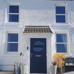 White Quickslide sliding sash windows on a white rendered house with a dark blue front door.