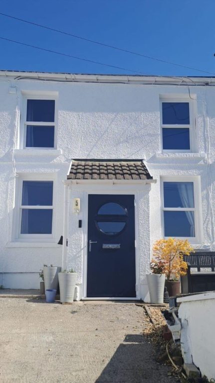 White Quickslide sliding sash windows on a white rendered house with a dark blue front door.